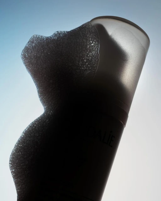 Close-up studio shot of a cylindrical frosted bottle expelling foam, showcasing texture against a graded blue and white backdrop.