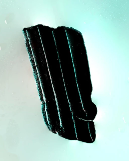 Dark, corrugated material fragment on a mint-green background, with sharp lines, texture, and shadows creating visual interest.