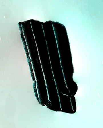 Dark, corrugated material fragment on a mint-green background, with sharp lines, texture, and shadows creating visual interest.