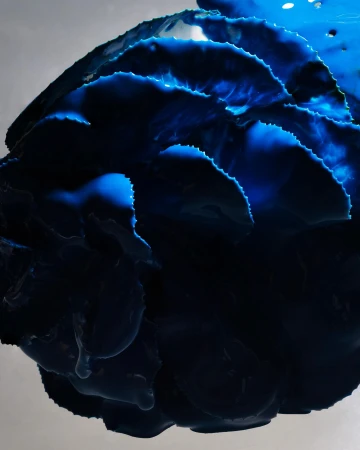 Dramatic close-up of blue ink-like liquid swirling and layered, creating an abstract, textural, and vibrant composition.