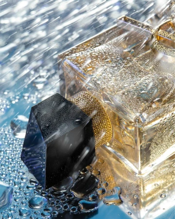 Close-up perfume bottle with faceted black cap under falling water droplets on reflective blue surface