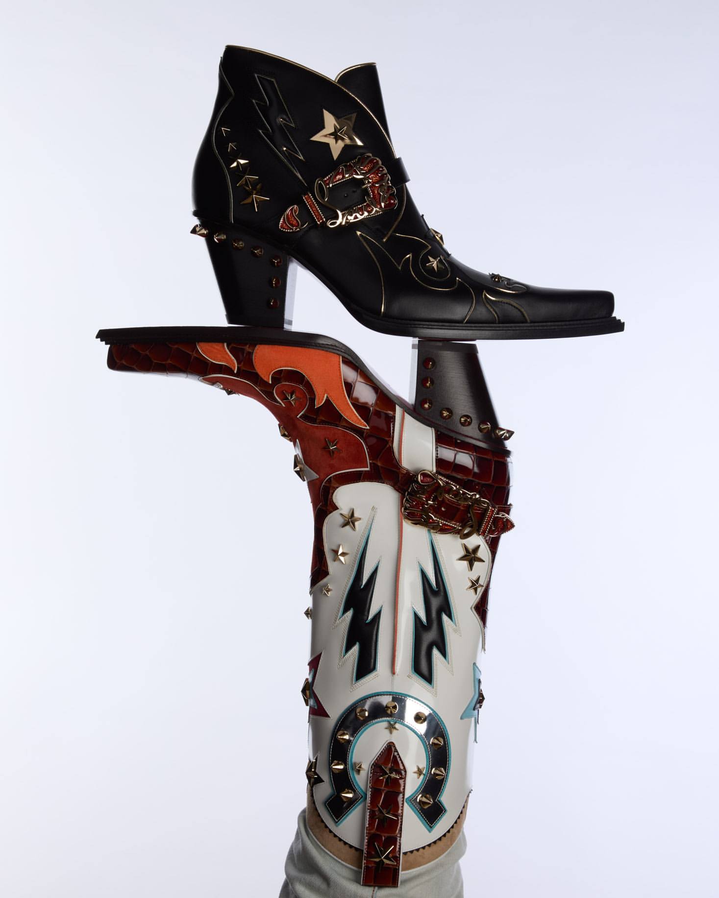 Two ornately decorated leather ankle boots are displayed against a white background, showcasing a blend of Western and edgy designs.