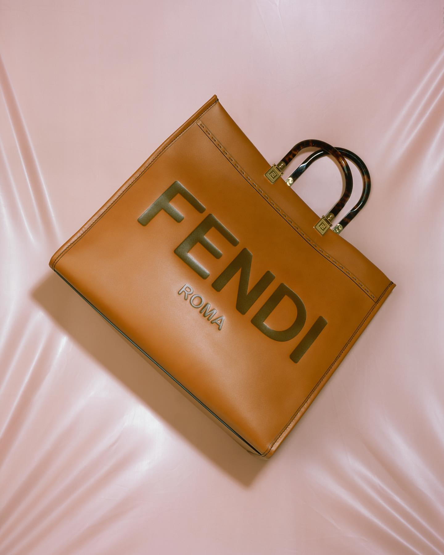 Fendi Roma brown leather tote bag with tortoise handles on a pink satin background, product shot for fashion and style.
