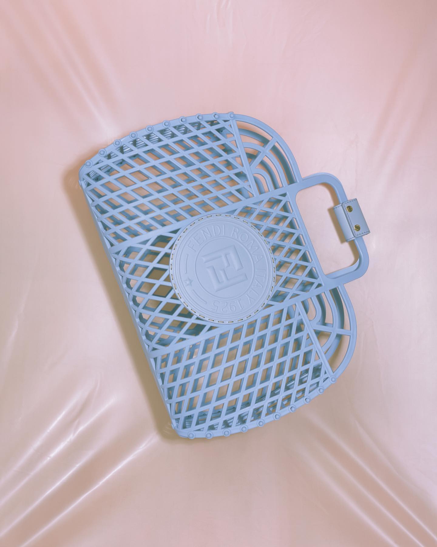 Light blue plastic tote bag with a circular logo detail on a soft peach colored background with subtle textures and folds. Close-up shot.