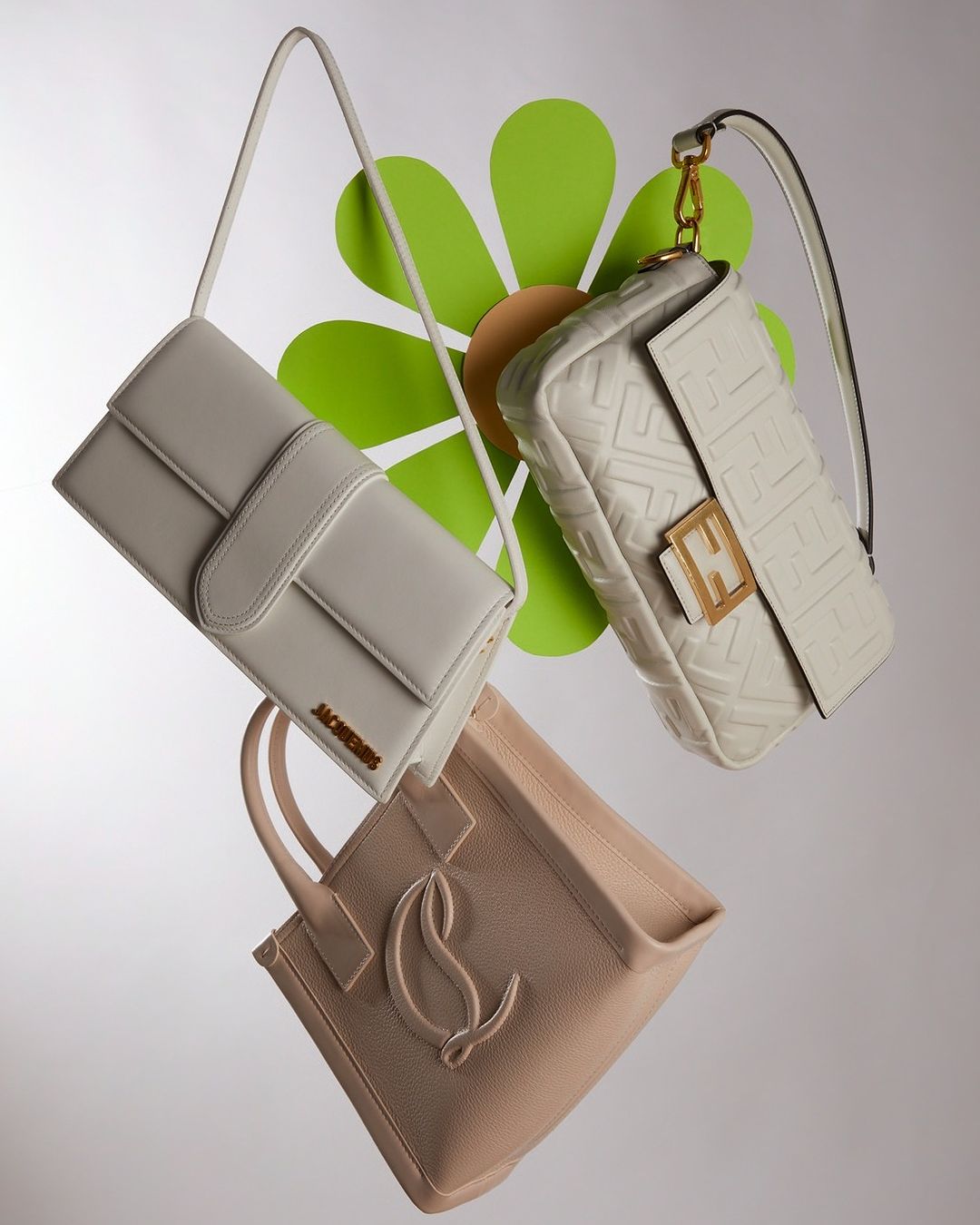 Three designer handbags are displayed against a white background with a decorative green flower. Bags vary in shape, size, and color. 