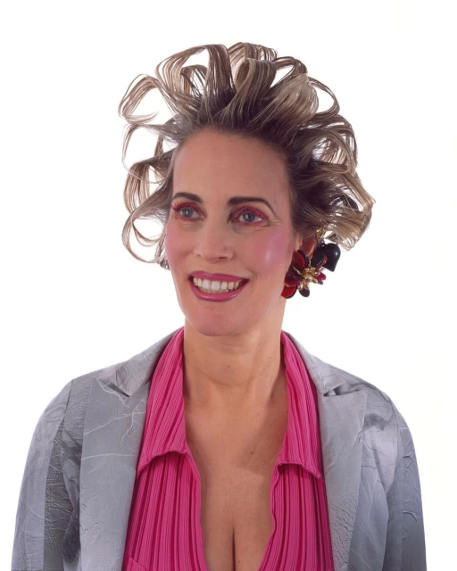 Smiling woman in a silver blazer and pink blouse against a white background with styled curly hair and floral earrings.