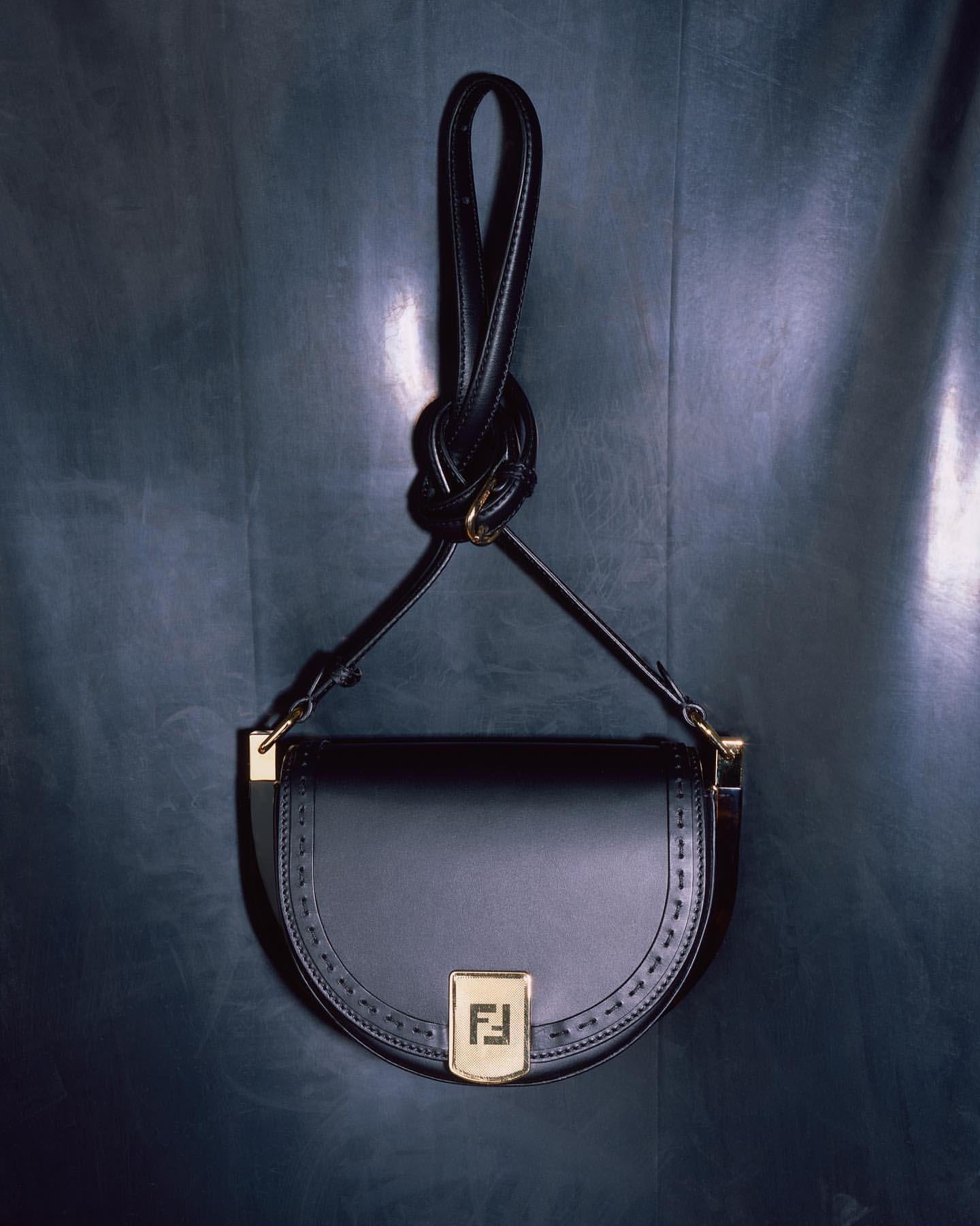 Elegant black leather Fendi handbag featuring the brand logo, gold hardware, and a distinctive looped handle against a dark backdrop.