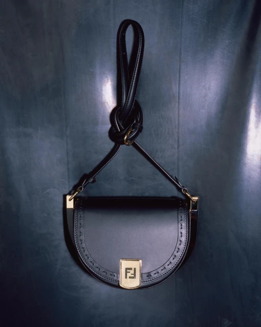 Elegant black leather Fendi handbag featuring the brand logo, gold hardware, and a distinctive looped handle against a dark backdrop.