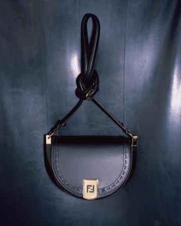 Elegant black leather Fendi handbag featuring the brand logo, gold hardware, and a distinctive looped handle against a dark backdrop.