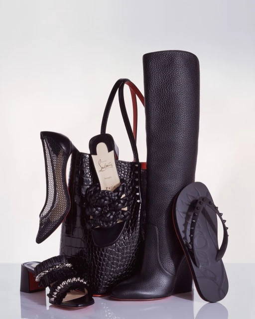 Arrangement of black Christian Louboutin shoes, boots, handbag, and sandal on a white surface, showcasing luxury fashion accessories.