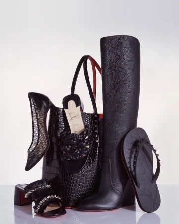 Arrangement of black Christian Louboutin shoes, boots, handbag, and sandal on a white surface, showcasing luxury fashion accessories.