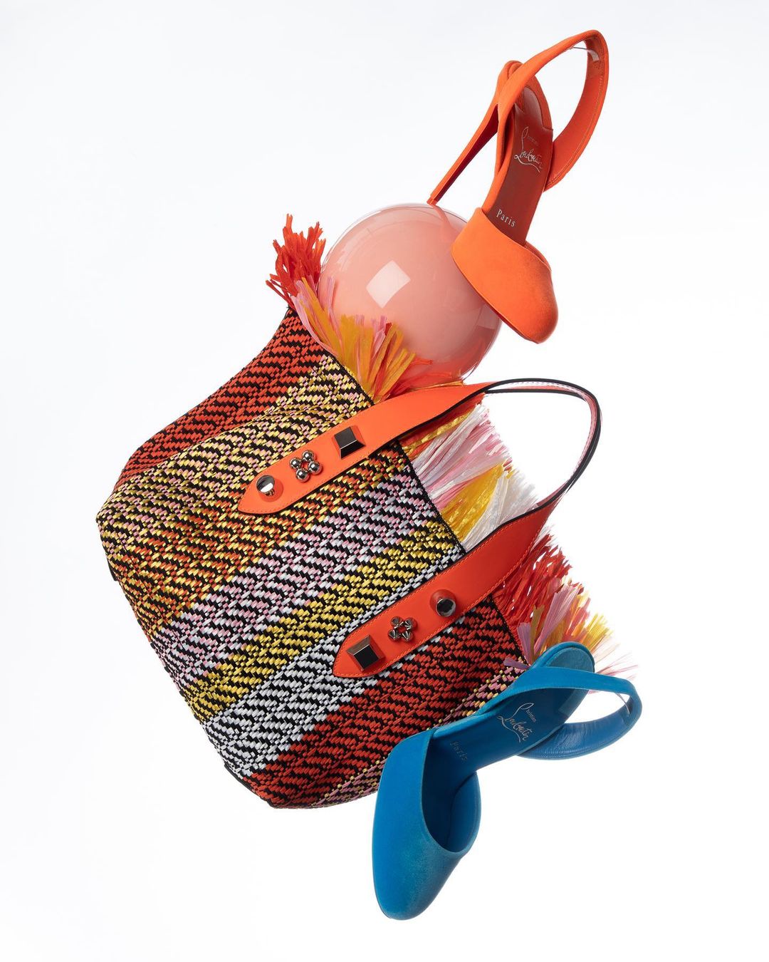 Striped woven tote bag with orange and blue high heel slingbacks floating in a white studio setting. Fashion-forward footwear and accessories.
