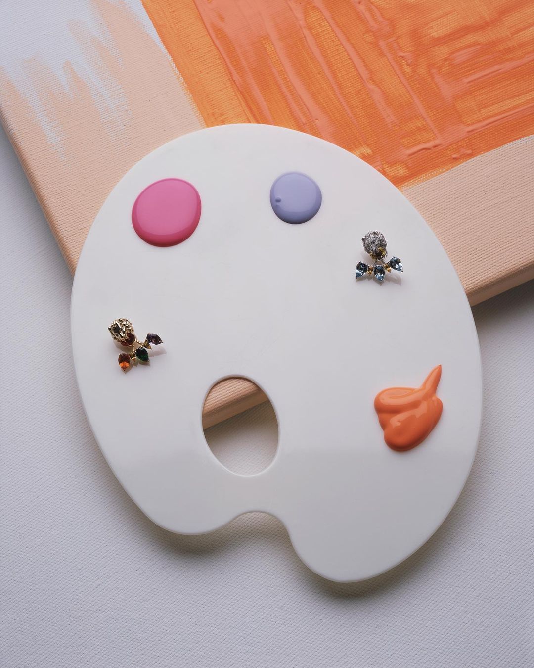 Art palette close-up with pink, purple, and orange paint dollops and toy figurine accents against a pastel canvas backdrop.