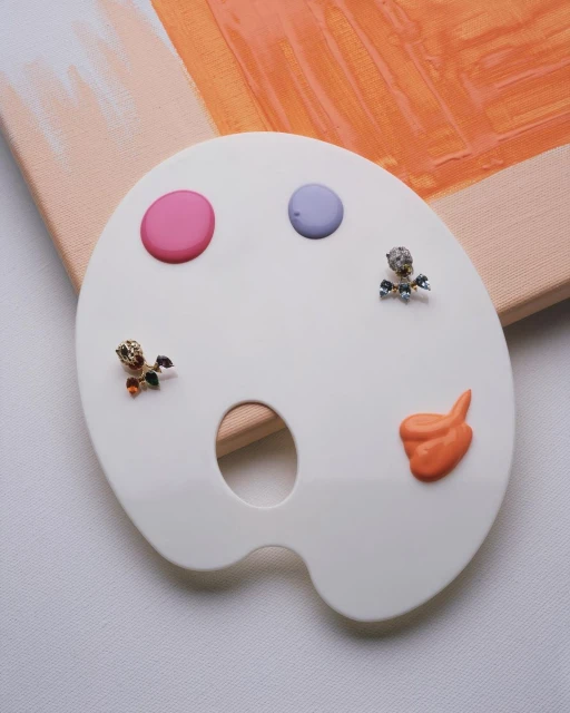 Art palette close-up with pink, purple, and orange paint dollops and toy figurine accents against a pastel canvas backdrop.