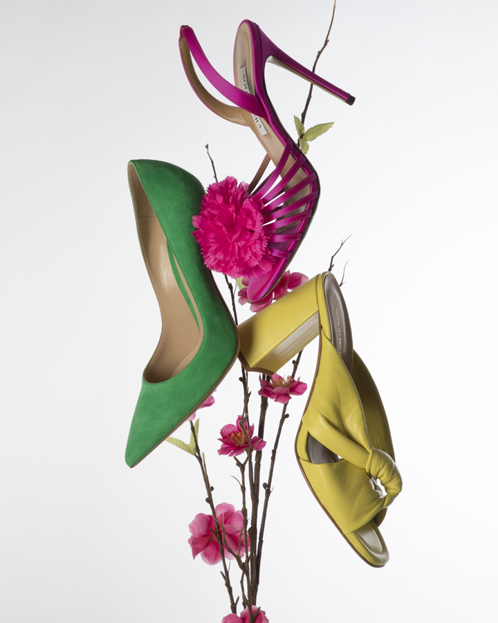 Arrangement of colorful high-heeled shoes with floral accents on a white background, showcasing fashion footwear.