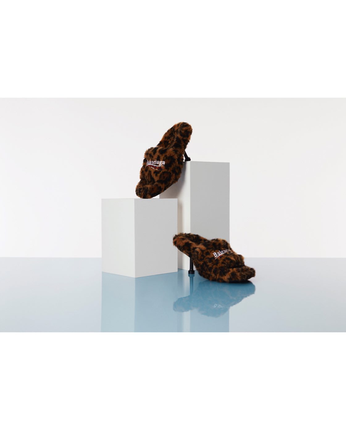 Two high-heeled shoes with a leopard print design displayed on white cube platforms against a gradient blue and white background.