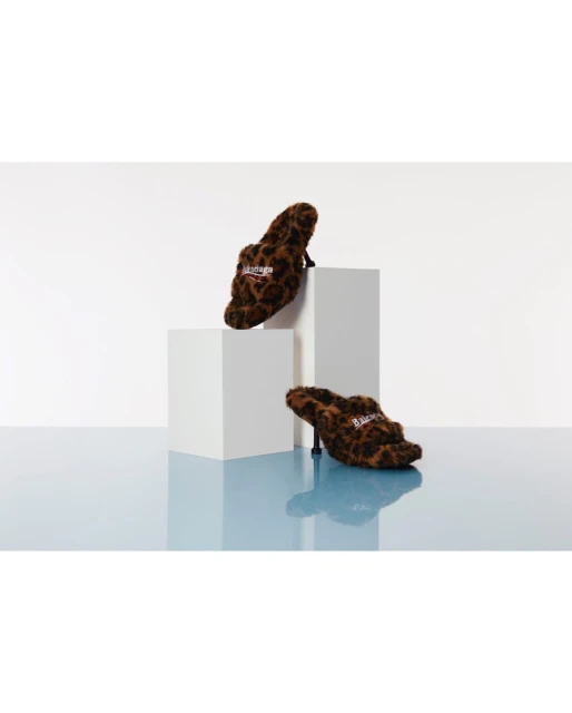 Two high-heeled shoes with a leopard print design displayed on white cube platforms against a gradient blue and white background.