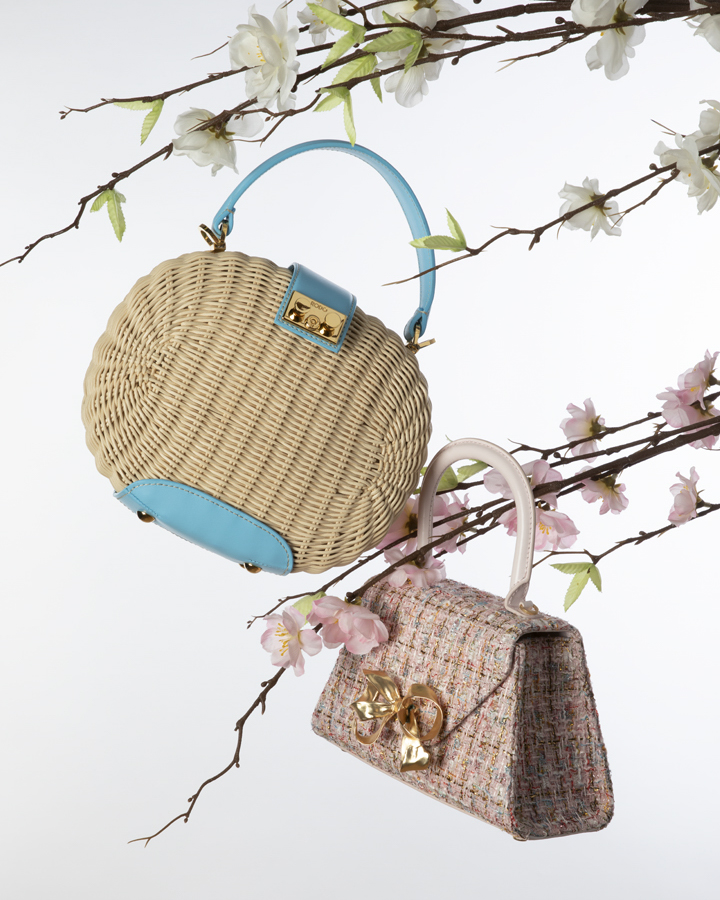 Two elegant handbags are displayed among cherry blossom branches against a clean white backdrop, showcasing fashion accessories.