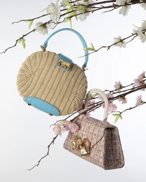 Two elegant handbags are displayed among cherry blossom branches against a clean white backdrop, showcasing fashion accessories.