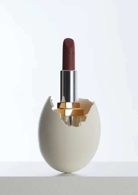 A lipstick standing in a cracked eggshell against a gradient white backdrop in a beauty advertisement concept.