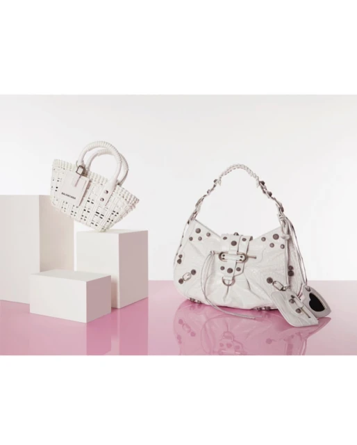 Two white Balenciaga handbags on white pedestals against a white and pink background, showcasing fashion and design elements.