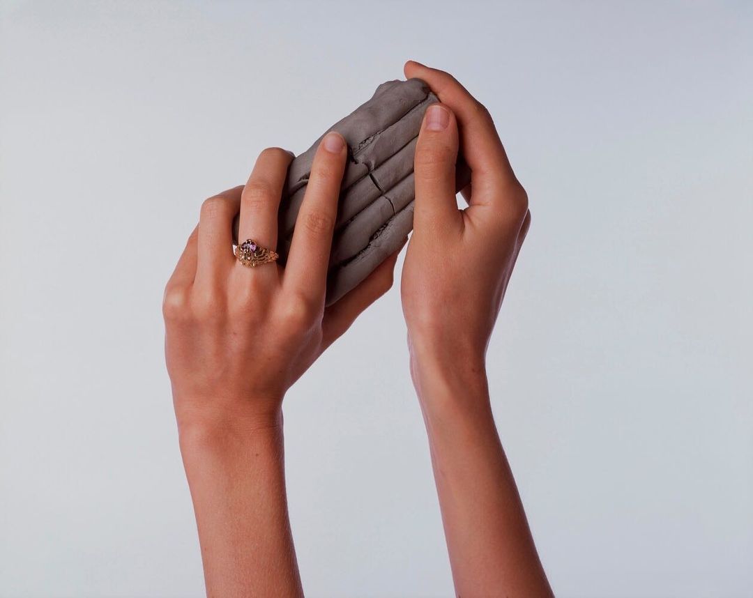Close-up shot of adult female hands holding gray clay, showcasing a ring on her left hand against a solid white background.
