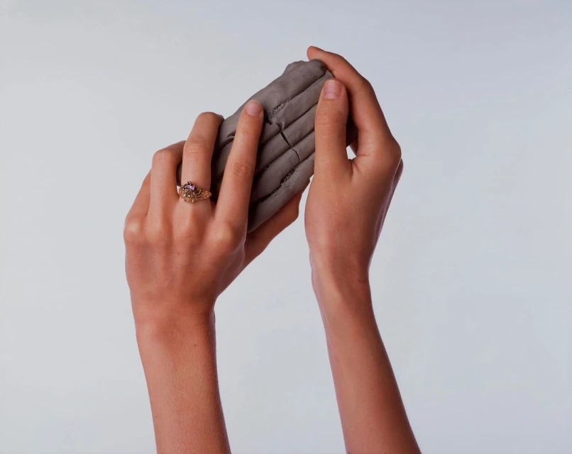 Close-up shot of adult female hands holding gray clay, showcasing a ring on her left hand against a solid white background.