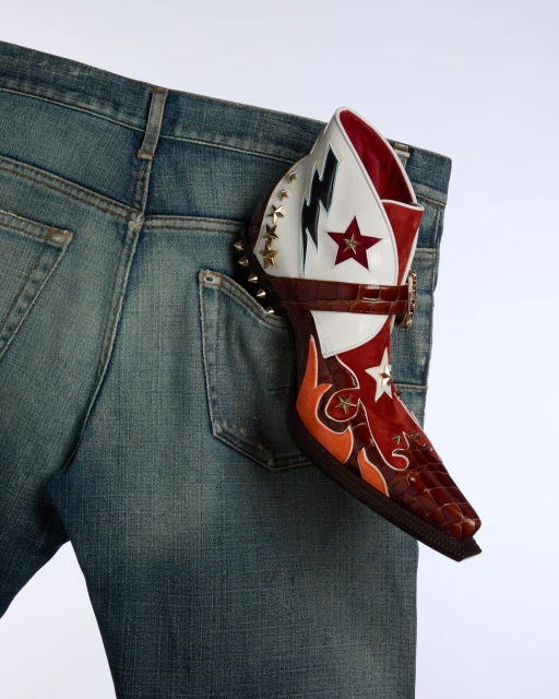 Denim jean with a colorful, patterned heeled boot sticking out of the back pocket on a white background. Fashion product shot.