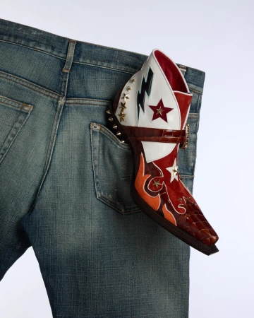 Denim jean with a colorful, patterned heeled boot sticking out of the back pocket on a white background. Fashion product shot.