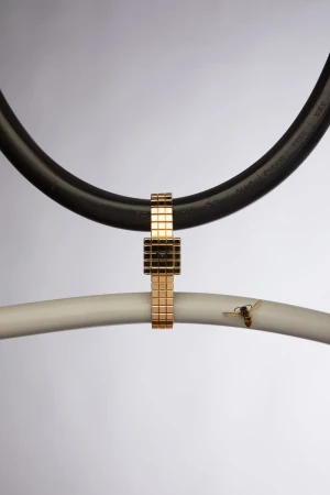 Gold wristwatch suspended between curved black and white pipes in a studio shot with a bee alighting on the white pipe.