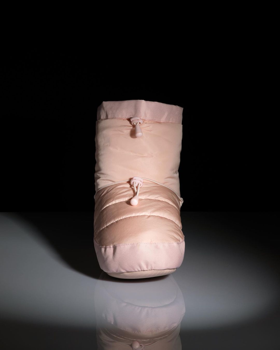 Close-up studio shot of a puffy ballet slipper, in pale pink color, reflecting on glossy surface with dark background.