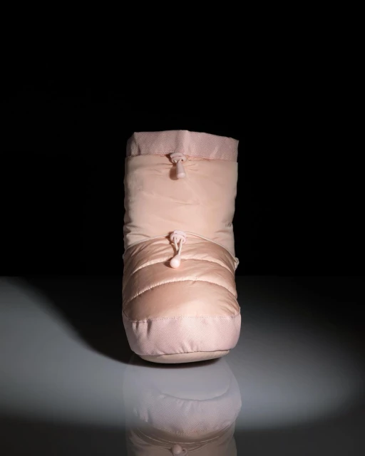 Close-up studio shot of a puffy ballet slipper, in pale pink color, reflecting on glossy surface with dark background.