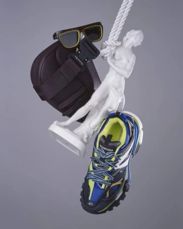 Fashion still life featuring sunglasses, brown purse, a white sculpture, a Balenciaga sneaker, and a white rope on a grey backdrop.