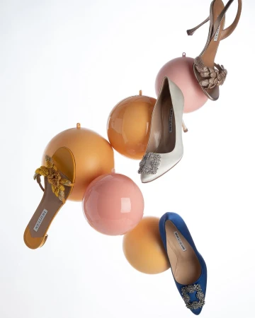 Arrangement of four different designer high heels with decorative buckles and embellishments, floating against a plain white backdrop.
