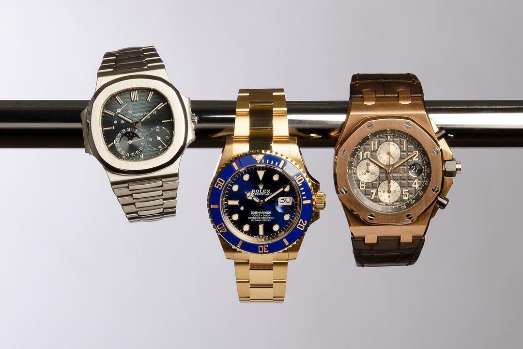 Three luxury wristwatches, including Rolex Submariner, displayed on metal bar. Close-up studio shot showcases the craftsmanship and design.