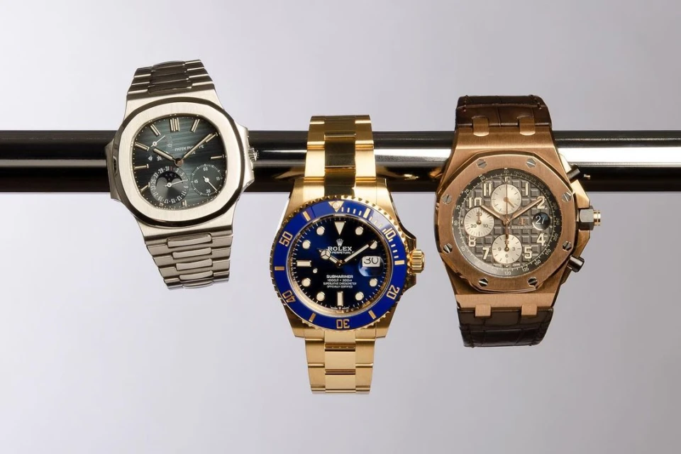Three luxury wristwatches, including Rolex Submariner, displayed on metal bar. Close-up studio shot showcases the craftsmanship and design.