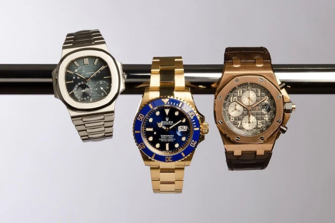 Three luxury wristwatches, including Rolex Submariner, displayed on metal bar. Close-up studio shot showcases the craftsmanship and design.