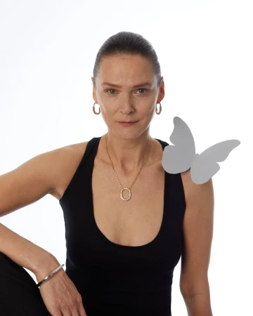 Portrait of a woman with hoop earrings and a gold necklace, black tank top, and a butterfly prop against a white backdrop.