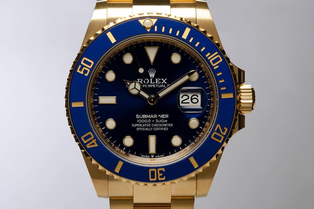 Close-up of a gold Rolex Submariner watch with a blue bezel and face, displaying the date and featuring the Rolex logo at the top.