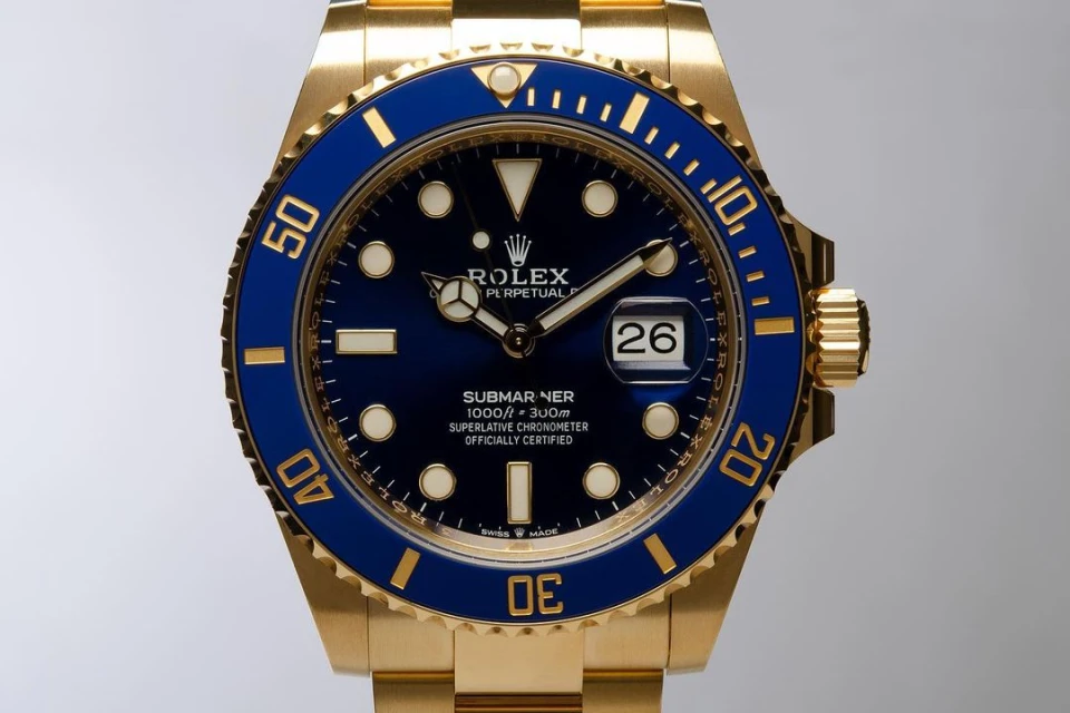 Close-up of a gold Rolex Submariner watch with a blue bezel and face, displaying the date and featuring the Rolex logo at the top.