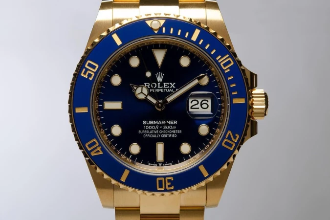 Close-up of a gold Rolex Submariner watch with a blue bezel and face, displaying the date and featuring the Rolex logo at the top.