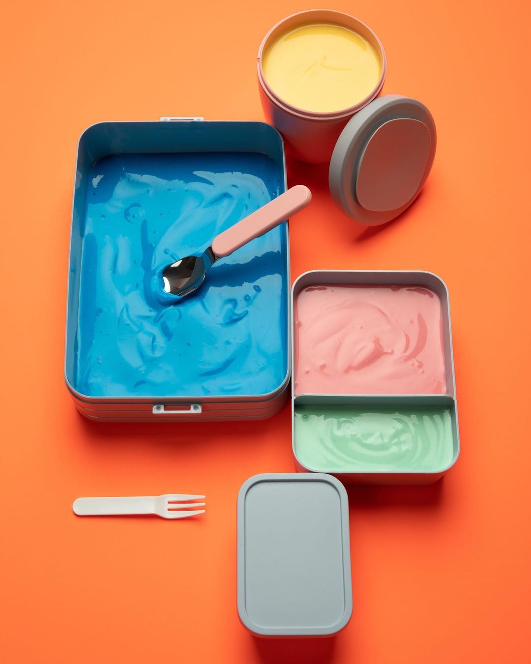 Colorful containers filled with brightly-colored sauces and dips, presented on a vivid orange backdrop, showcasing food storage.