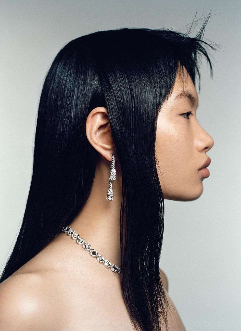 Profile shot of an Asian female wearing diamond jewelry with long black hair and fair skin, posing against a light grey background.