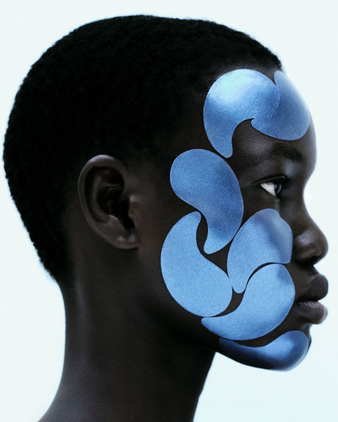 Profile of a black female model with blue face patches on a clean white background, demonstrating beauty and skincare application.