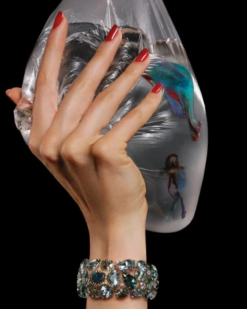 Elegant studio shot featuring a manicured hand holding a plastic bag with an exotic fish, adorned with a sparkling blue jeweled bracelet.