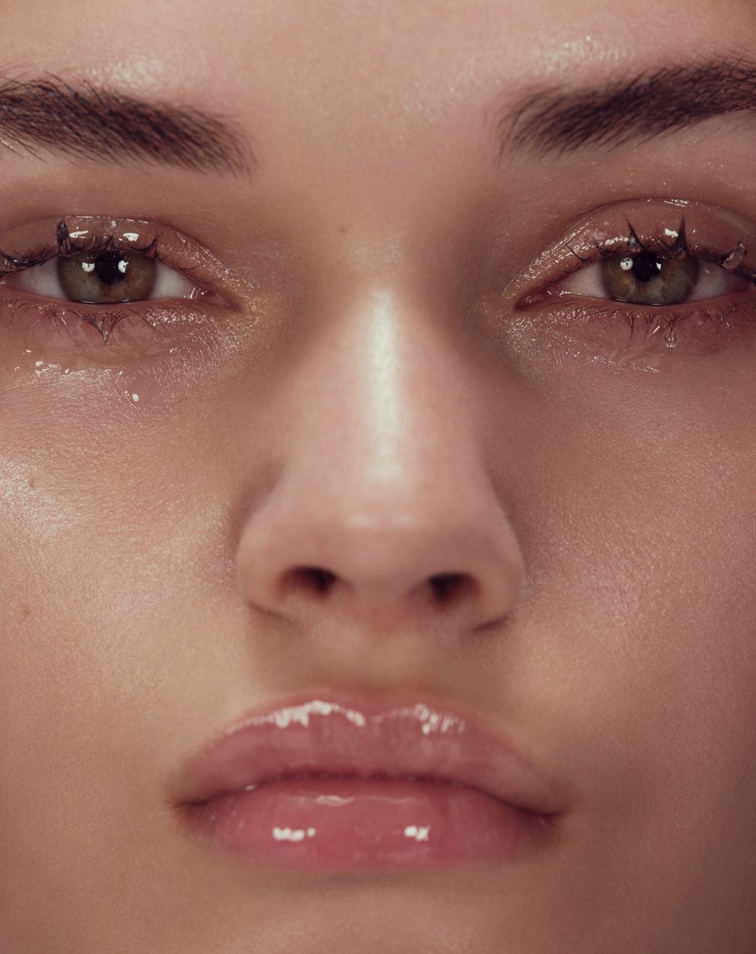 Extreme close up macro portrait of a model face focusing on glossy lips and dewy skin with detailed eyelashes.