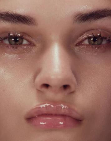Extreme close up macro portrait of a model face focusing on glossy lips and dewy skin with detailed eyelashes.