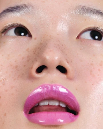 Close-up portrait of a woman with glossy pink lipstick and visible freckles shot from below by Antoine And Charlie