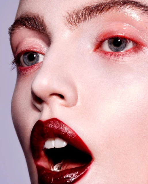 Close-up shot of a model's face with vibrant red eye makeup and glossy red lipstick, showcasing beauty and makeup details in a studio setting.