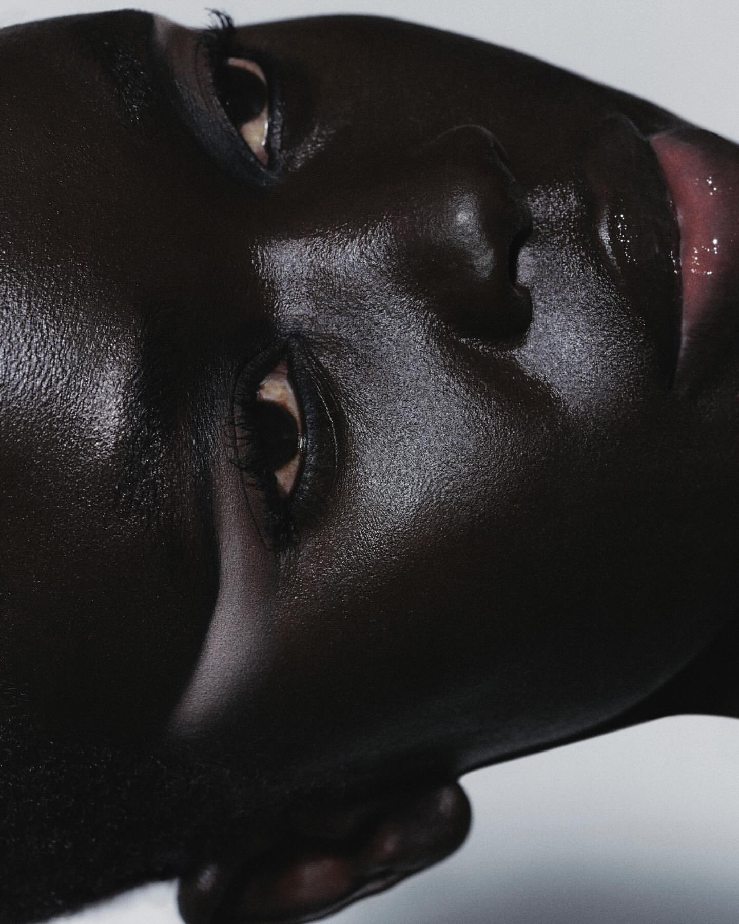Close-up portrait of a dark-skinned model with glossy skin and detailed eye makeup captured by Antoine And Charlie in Paris.